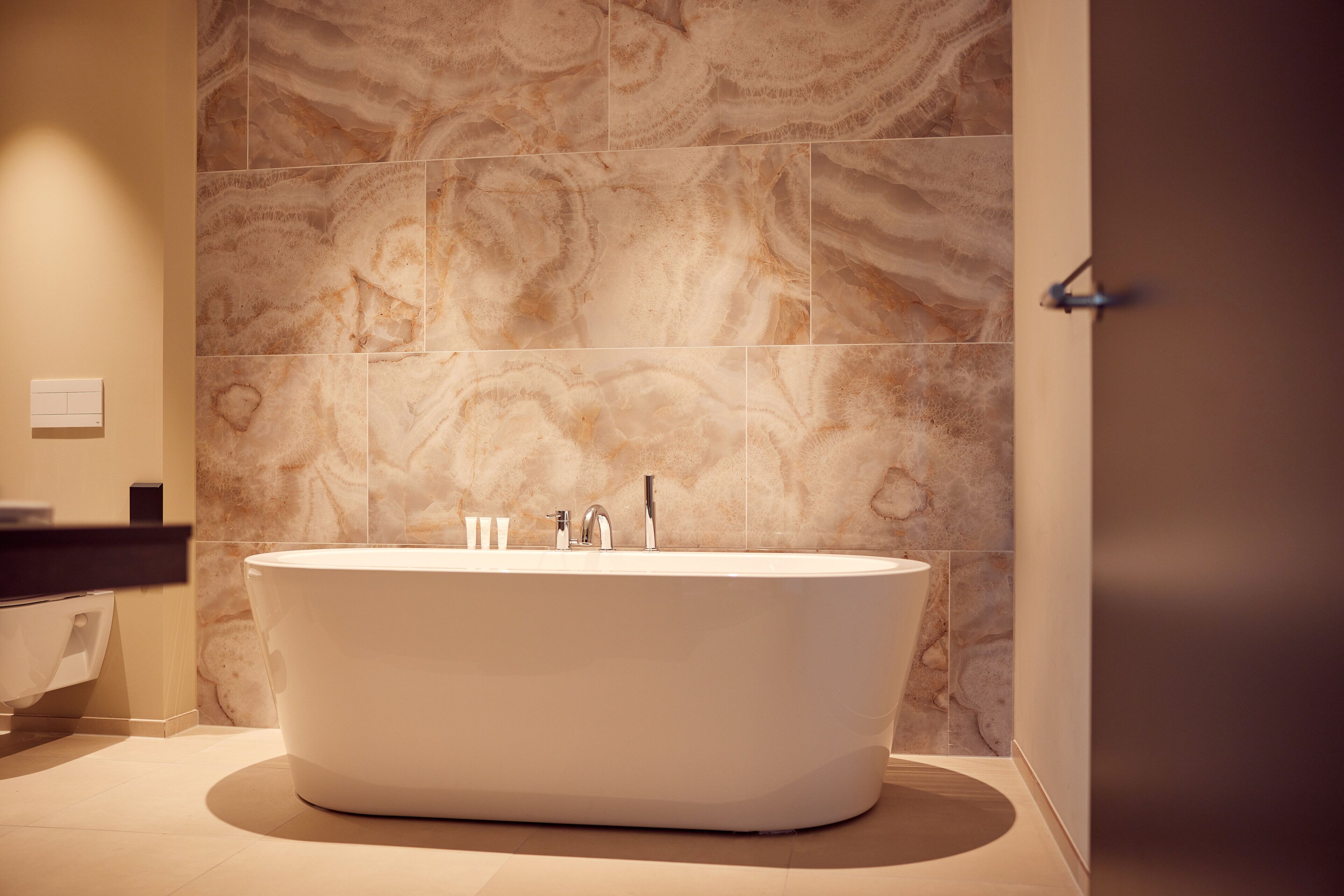 Une salle de bain moderne avec une baignoire sur pieds, des carreaux de marbre aux murs et un design minimaliste.
