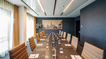 Une salle de conférence avec une longue table, des fauteuils en cuir marron et un tableau représentant un paysage urbain accroché au mur.