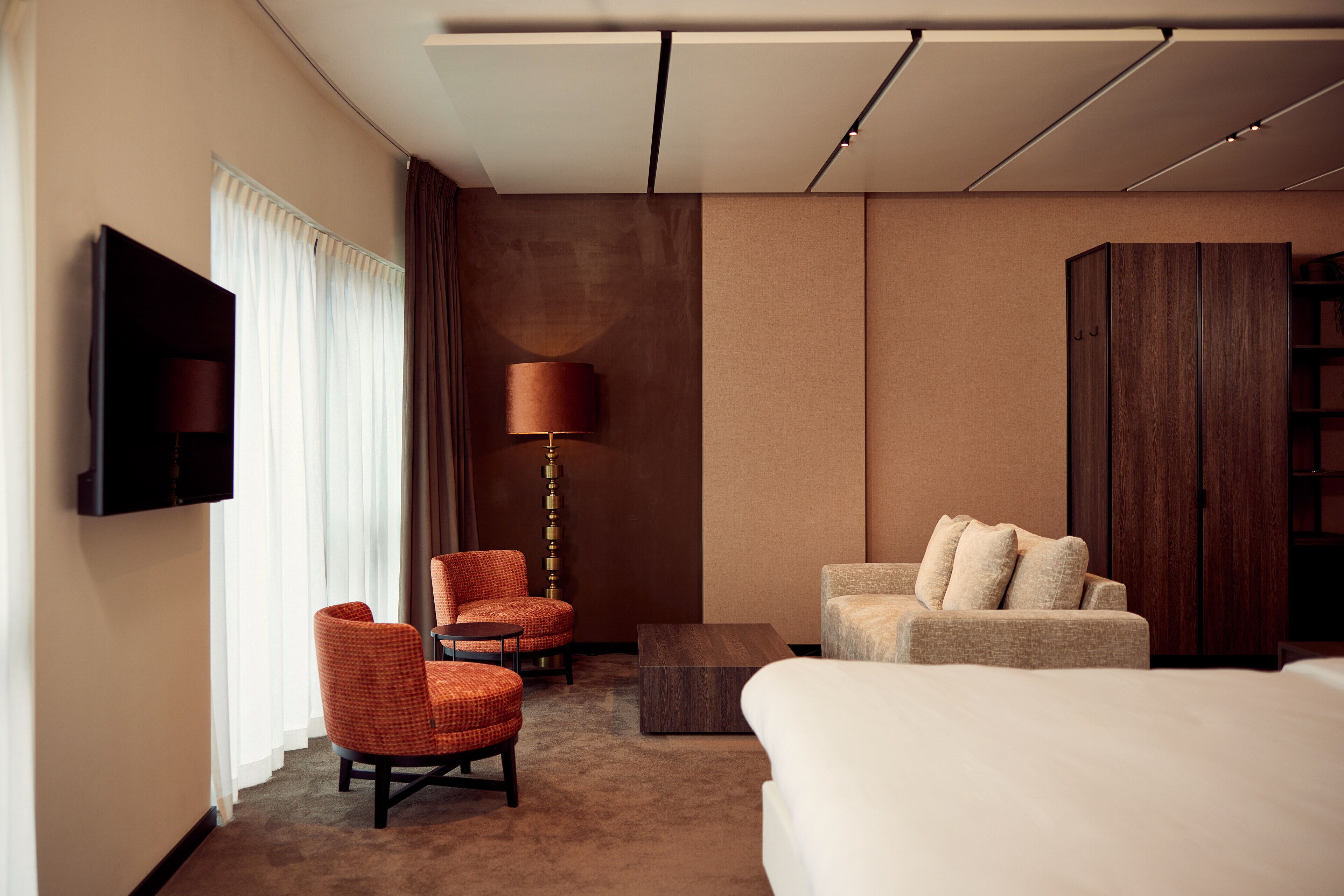 A hotel room with a bed, two armchairs, a sofa, a coffee table, a TV, and a lamp.