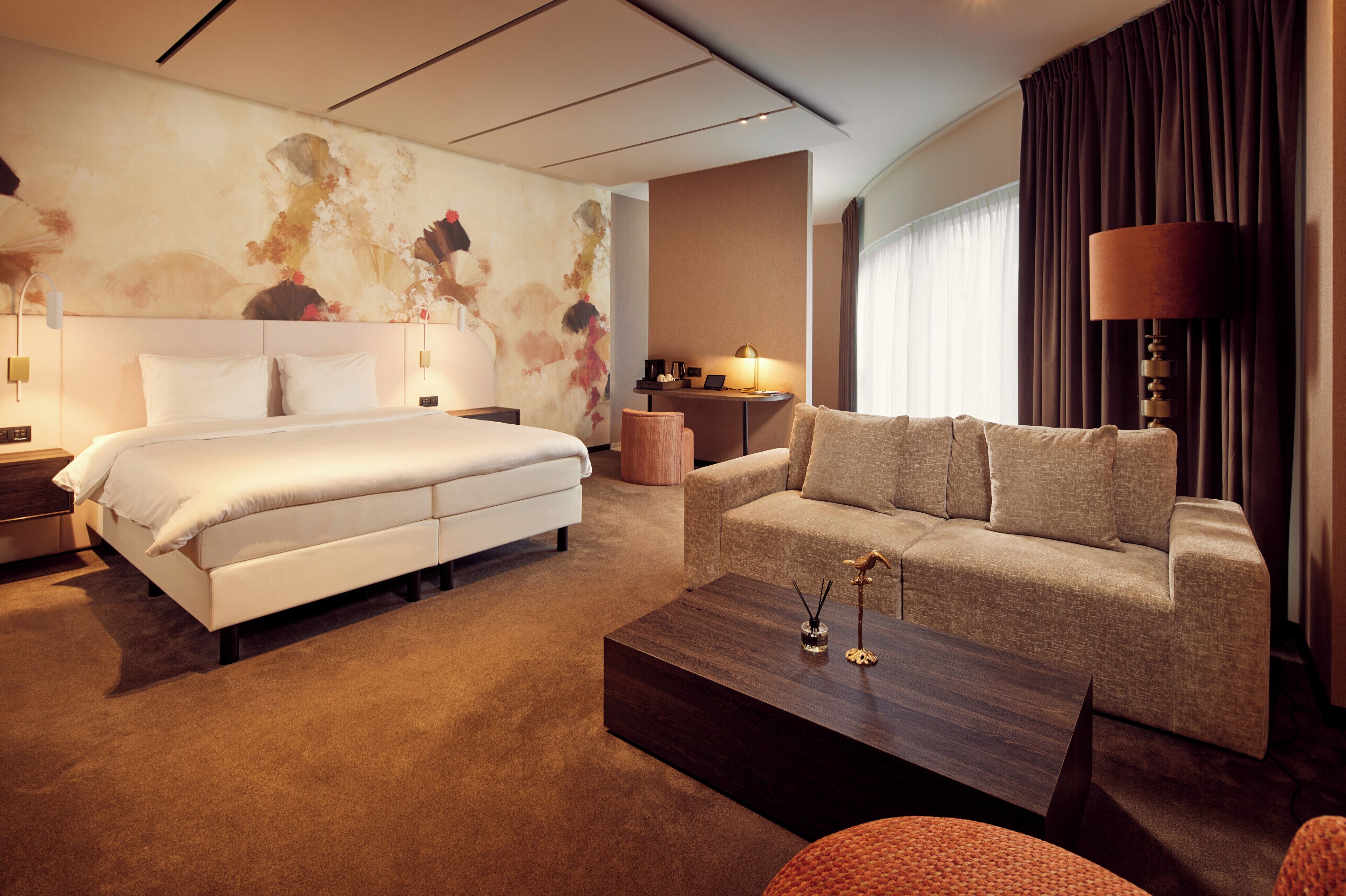 A hotel room with a bed, a sofa, a coffee table, and a lamp.