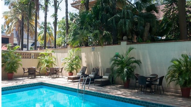 Una piscina con lettini e piante in vaso, circondata da alte palme.
