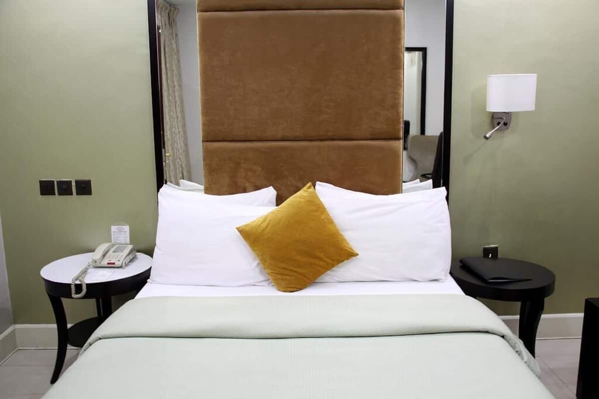Een hotelkamer met een bed, een nachtkastje met een telefoon, een tafeltje met een lamp en een spiegel aan de muur.