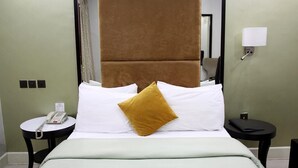 Una camera d'albergo con un letto, un comodino con il telefono e un abat-jour, e uno specchio a parete.