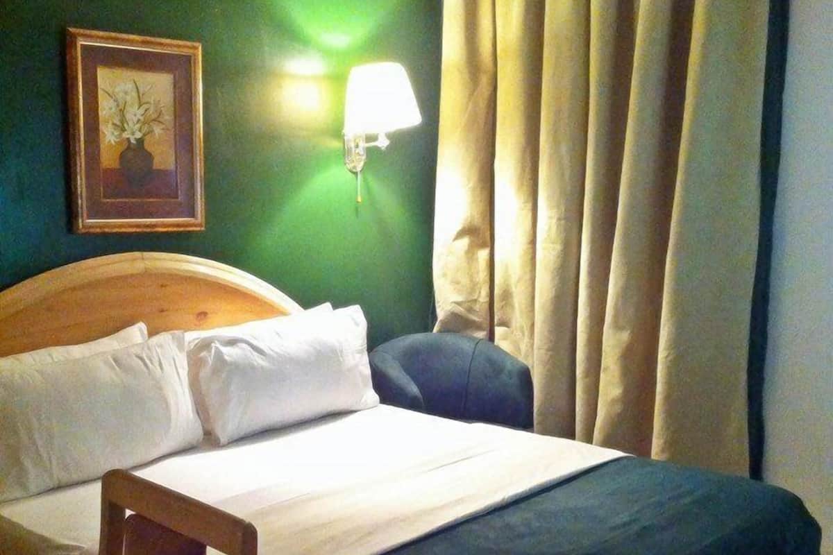 Een hotelkamer met een bed, een stoel, een lamp en een schilderij aan de muur.