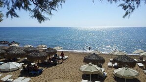 Una playa con tumbonas y sombrillas, vista despejada del mar, y algunas personas caminando.