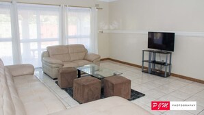 En stue med en beige sofa, et glasbord og et fjernsyn på et stativ.