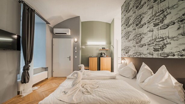 A hotel room with two beds, a flat-screen TV, an air conditioning unit, and a wall with a nautical-themed wallpaper. - easy-flat Neustiftgasse - AC Studio Apartments near MuseumsQuartier (Vienna)