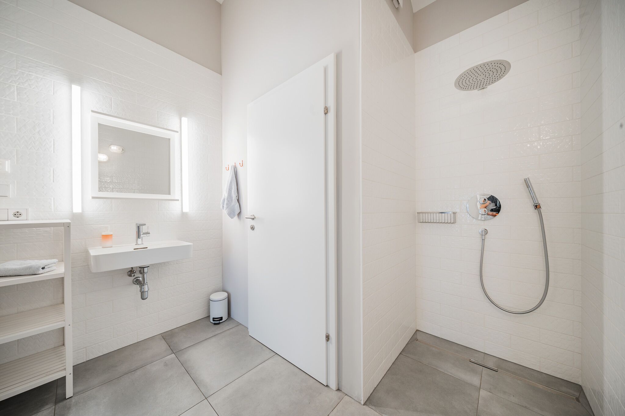 Een moderne badkamer met een wit wastafelmeubel, spiegel en douche.