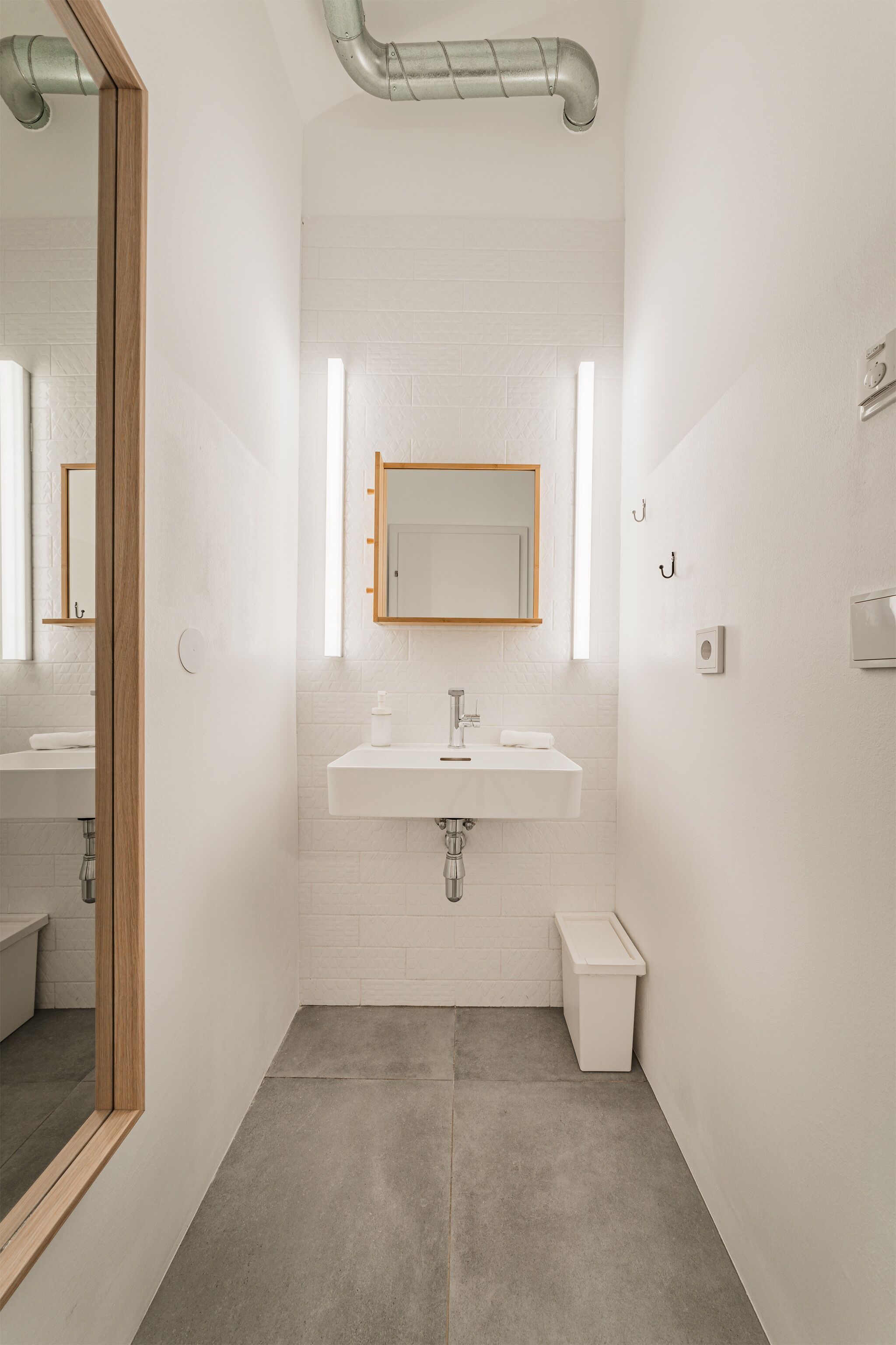 Un baño moderno con lavamanos blanco, espejo y piso de baldosas.