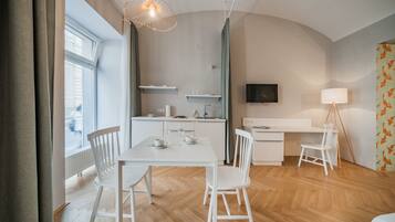 Een moderne, goed verlichte kamer met een eettafel, stoelen, een keukenhoek en een aan de muur bevestigde televisie.
