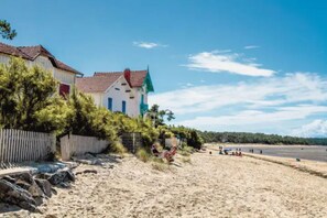 A beach with a white building with a red roof and a green roof. There are people on the beach and a fence in the foreground. - Vacation Home in Ronce-les-Bains (sleeps 6) Private Parking - Garden Terrace (La Tremblade)