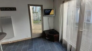 Une pièce avec une porte donnant sur l’extérieur, un téléviseur fixé au mur, une petite table et une prise de courant.