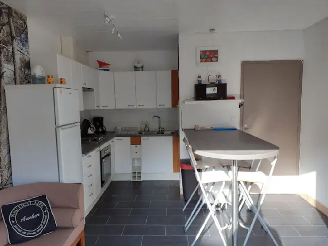 A compact kitchen with white cabinets, a dining table with chairs, a refrigerator, and a coffee machine.