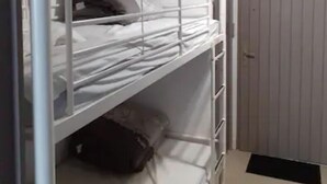 Une chambre avec des lits superposés, un gilet de sauvetage accroché au mur, une porte et un luminaire.