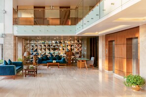 Eine großzügige Lobby mit hoher Decke, einer Sitzecke mit Sofas und einem Couchtisch, einer Wandverkleidung und einem Aufzug.