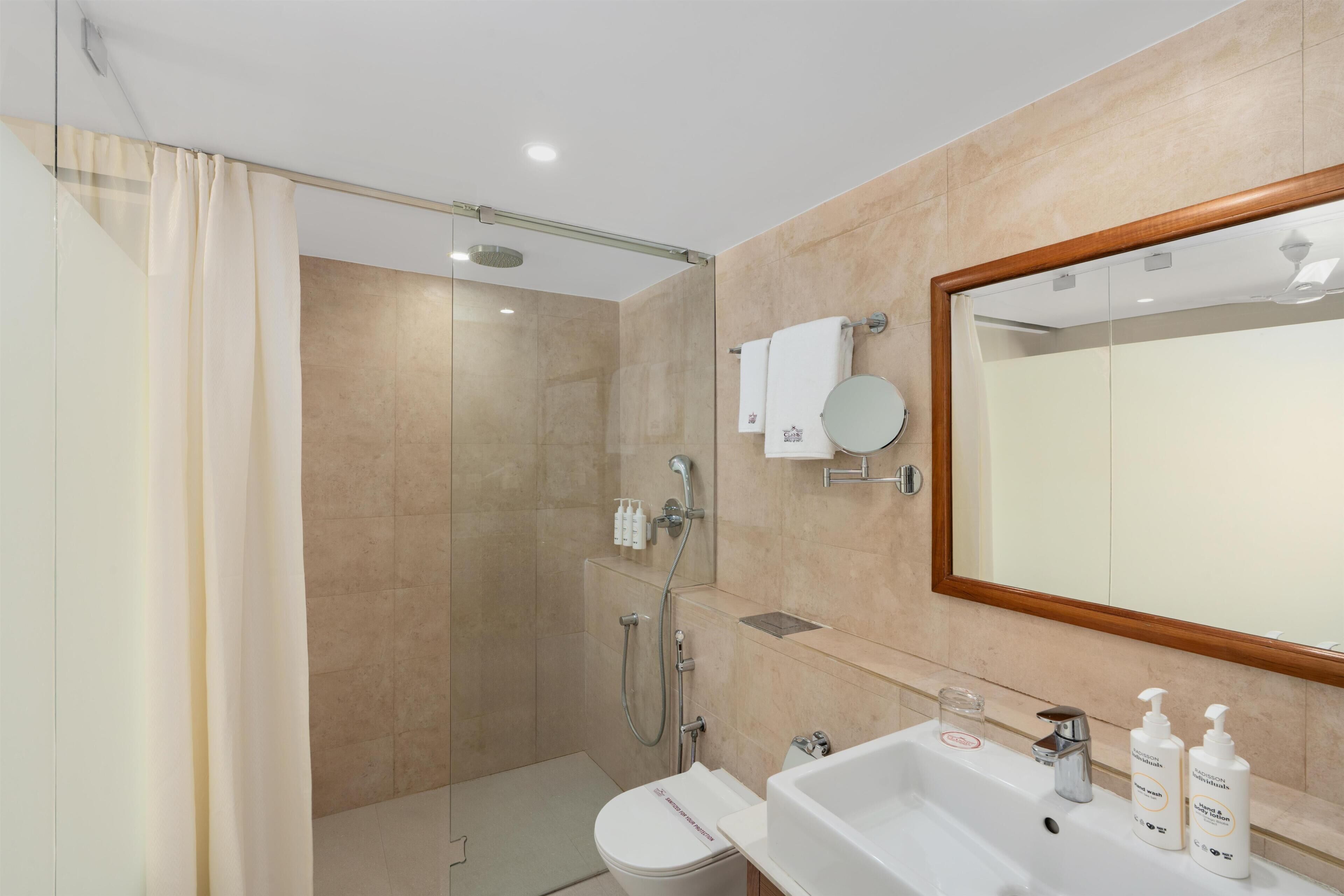 A modern bathroom with a shower, toilet, sink, and a large mirror.