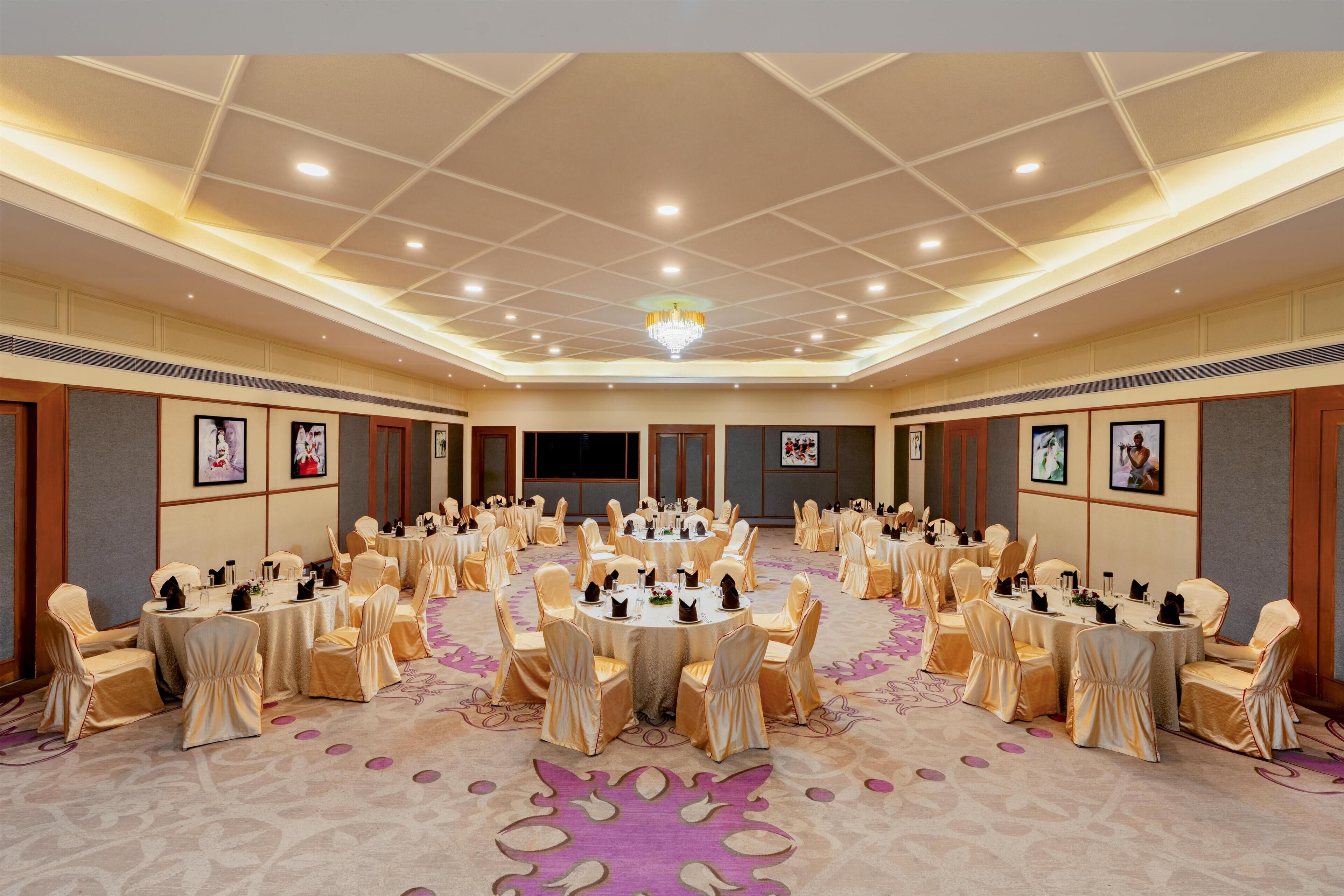 A large conference room with round tables and chairs, a chandelier, and framed pictures on the walls.