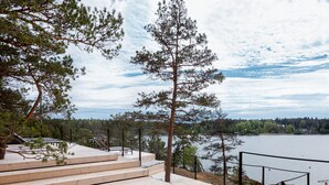 A wooden deck with steps leading to a bed, overlooking a lake with trees and a distant shoreline. - The Baro (Inga)