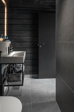 A modern bathroom with a white sink, dark wooden walls, and a tiled floor.