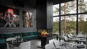 A modern dining area with a fireplace, green seating, and large windows overlooking trees. - The Baro (Inga)