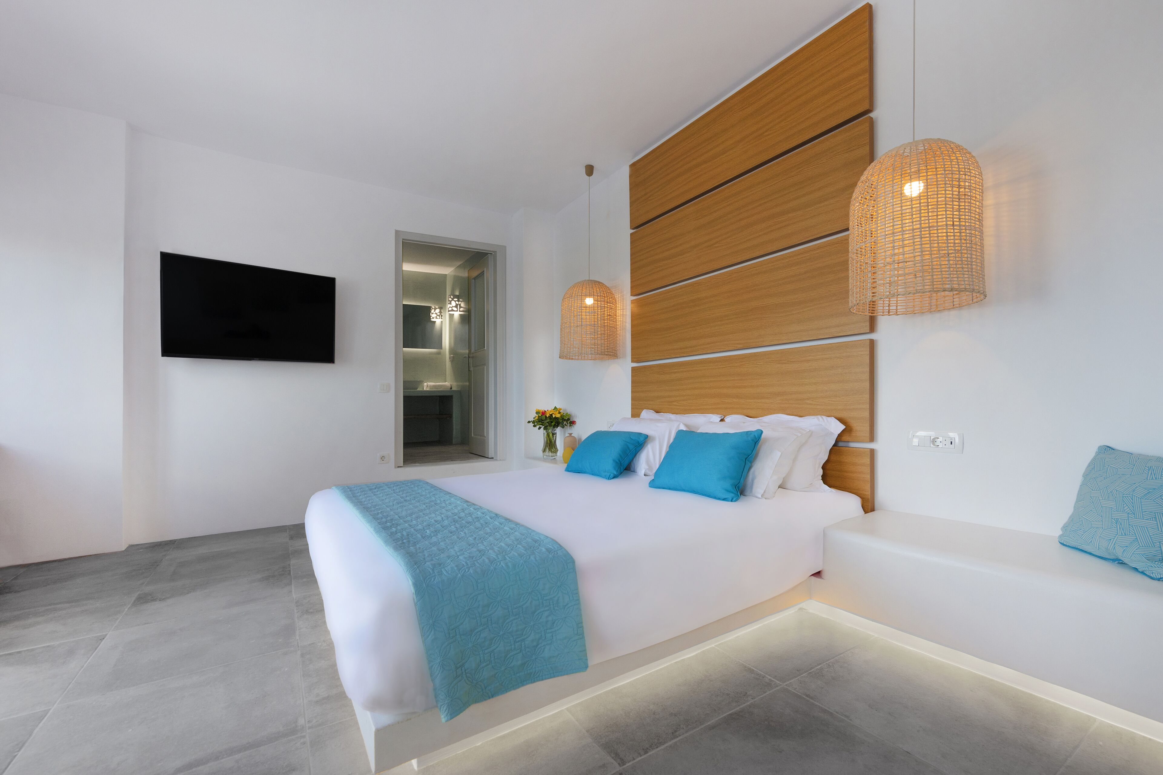 A modern bedroom with a large bed, a built-in bench, a TV mounted on the wall, and a wooden panel design on the wall.