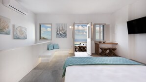 Un dormitorio moderno con una cama grande, un escritorio y vista al mar por una puerta abierta.