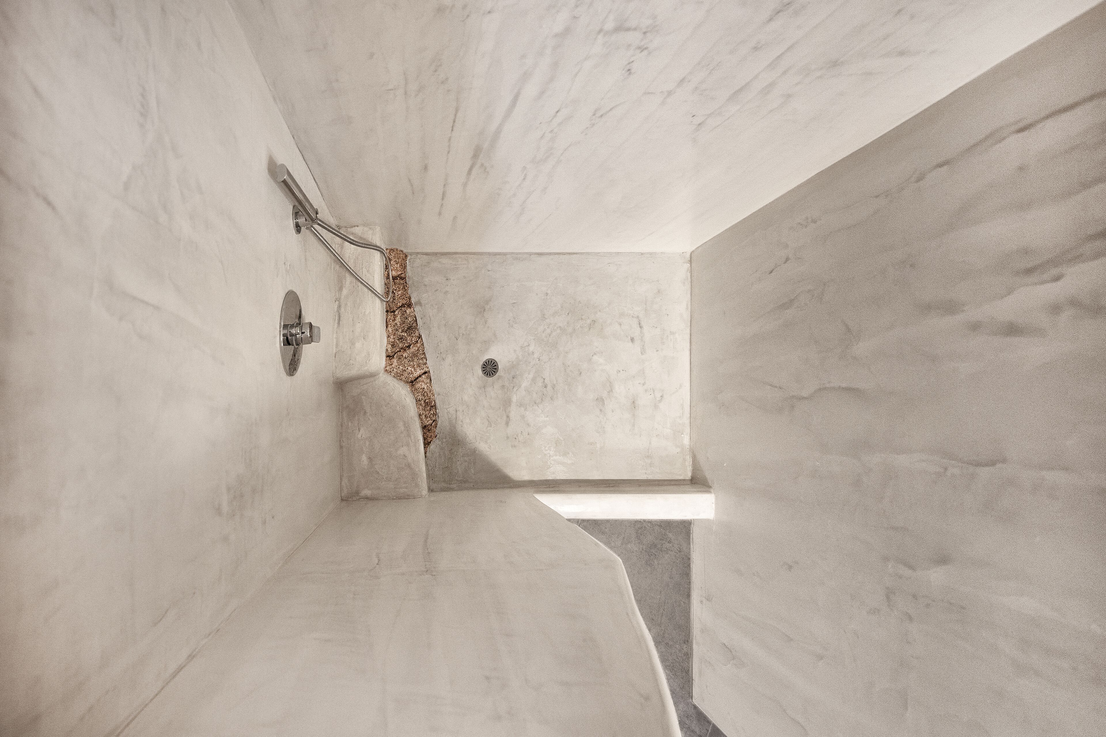 A modern bathroom with a marble floor, a shower area with a glass door, and a visible drain.