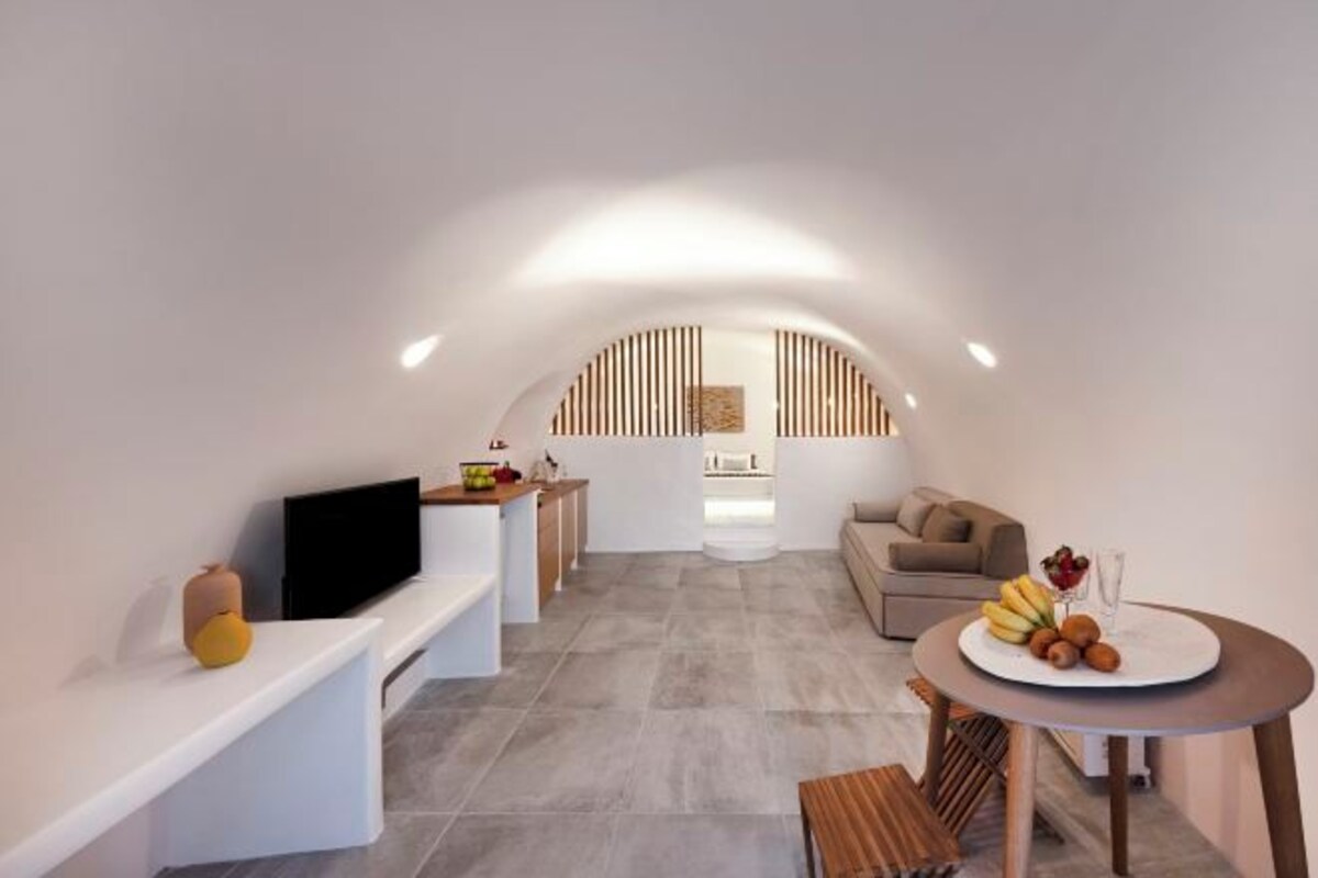 Ein moderner, offener Wohnbereich mit Flachbildfernseher, einem Esstisch mit Früchten und einer Couch.