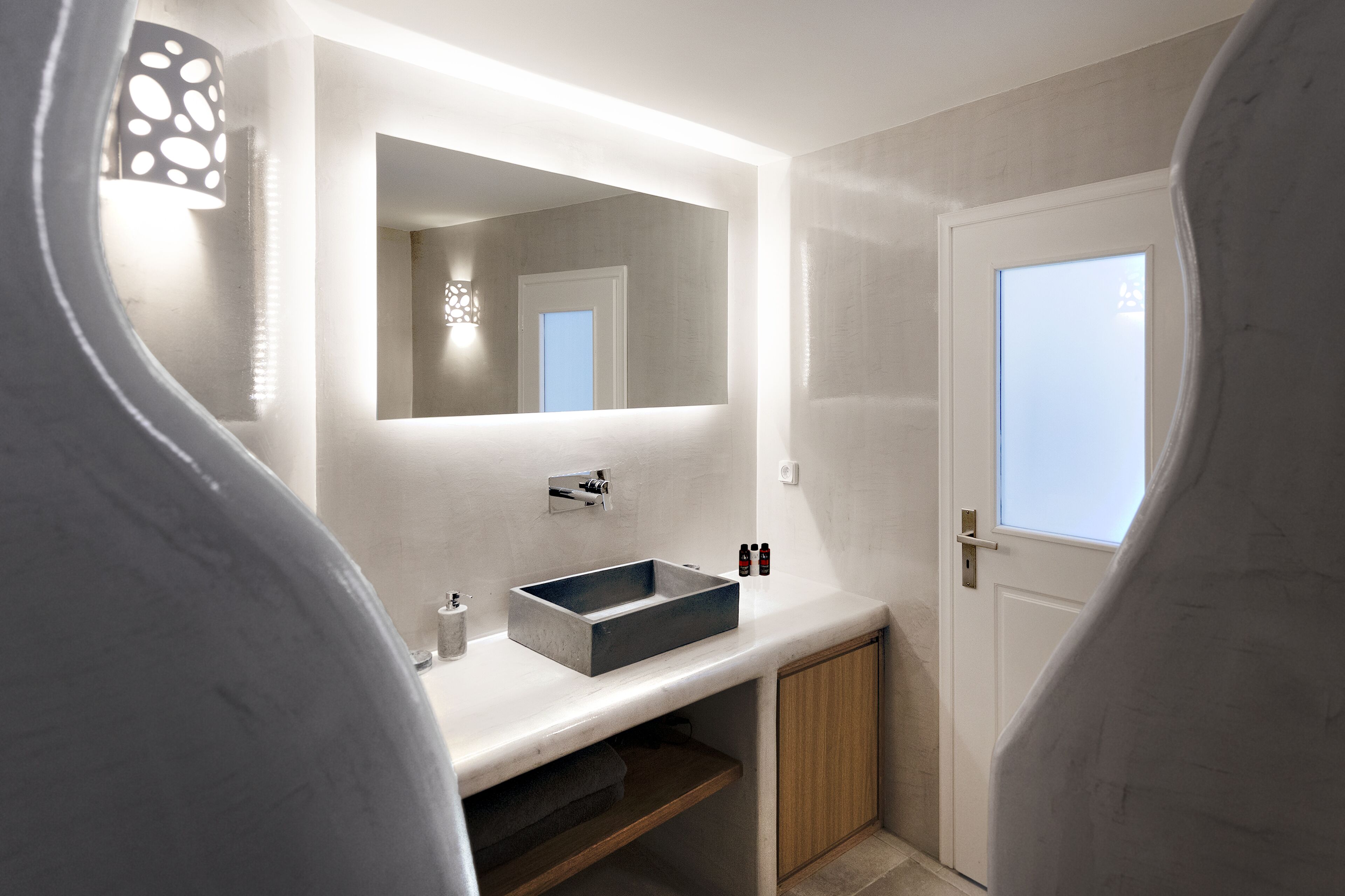 Ein modernes Badezimmer mit einem rechteckigen Waschbecken, einem Spiegel und einer Tür mit Milchglasfenster.