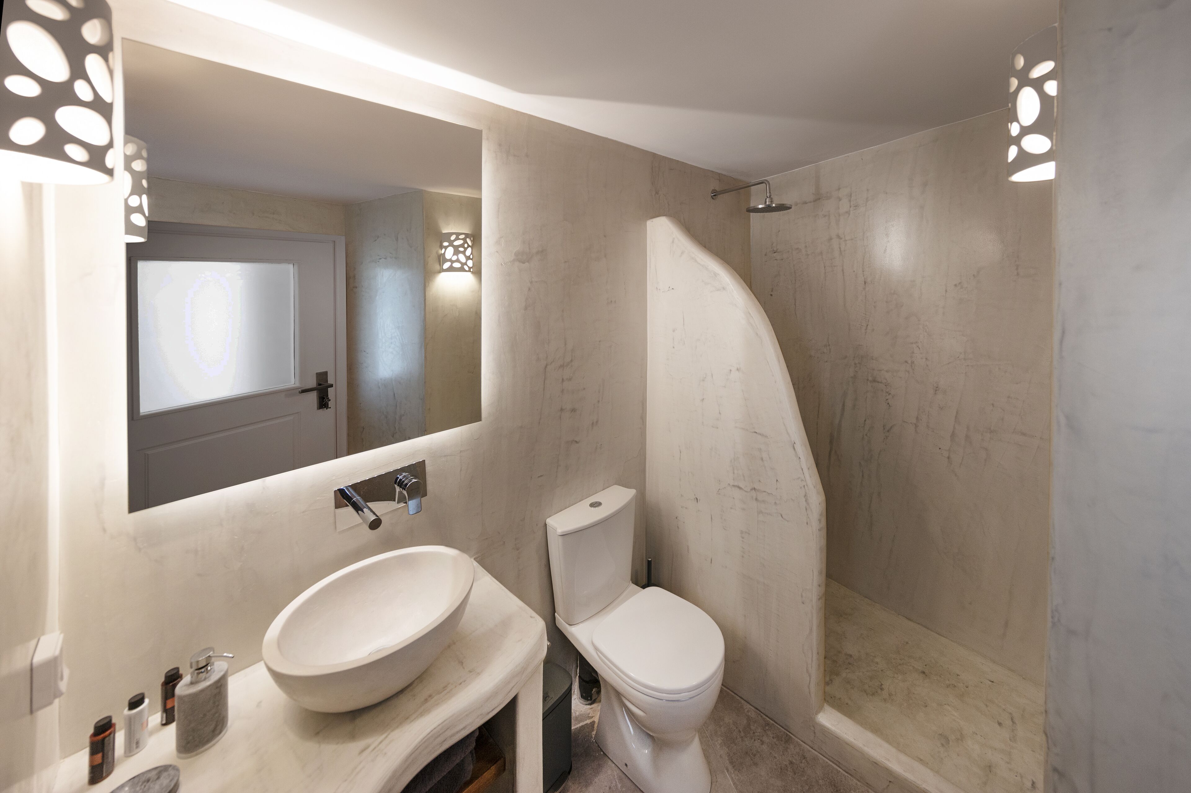 A modern bathroom with a large mirror, a round sink, a toilet, and a shower.