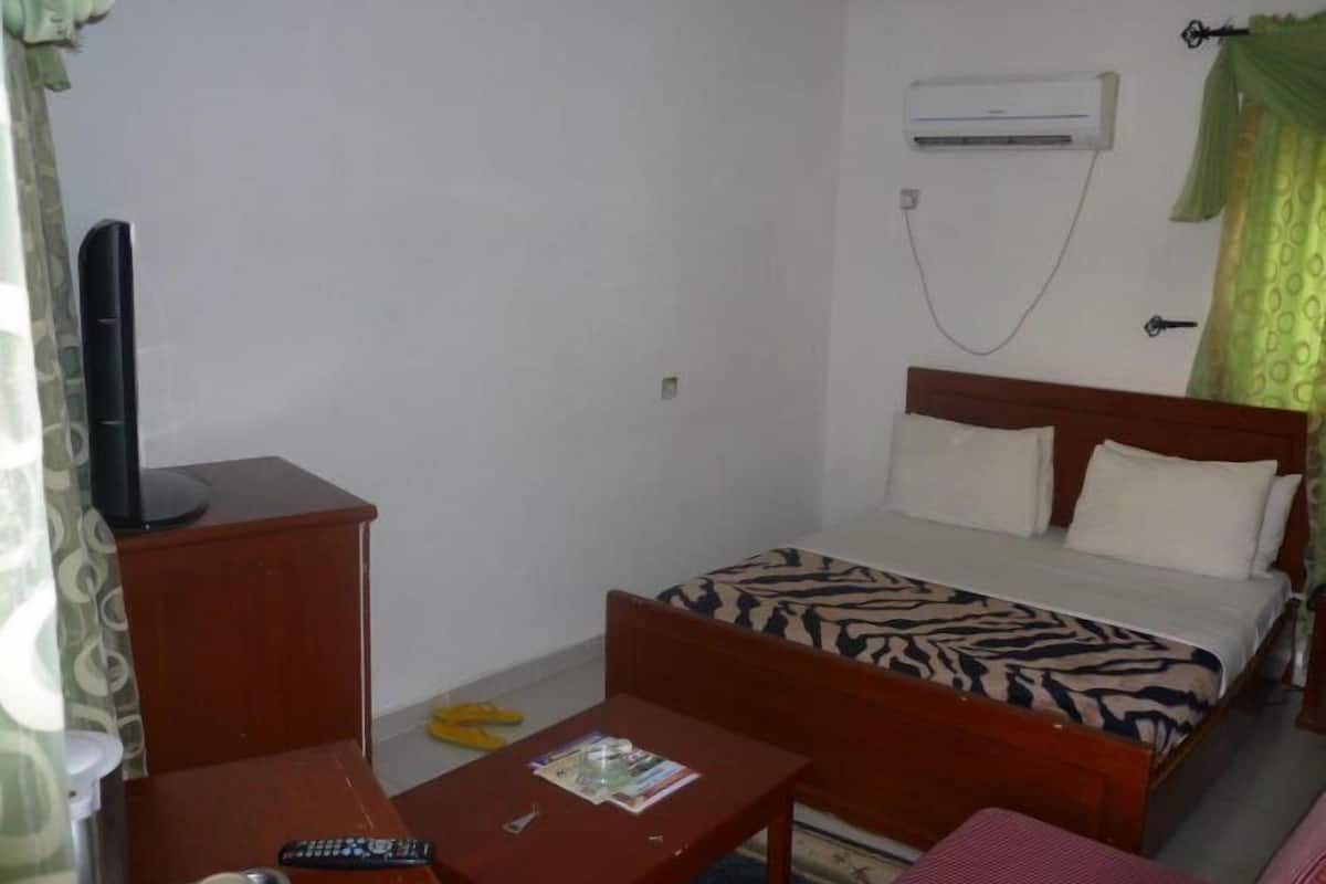Una habitación pequeña y sencilla con cama, escritorio, silla, televisor y aire acondicionado.