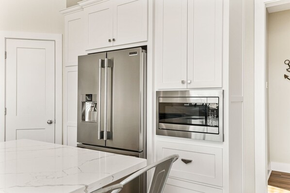 A modern kitchen with white cabinetry, a stainless steel refrigerator, and an integrated oven.