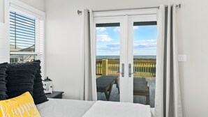 Quarto com cama, mesa de cabeceira, abajur e vista para a praia através de uma porta de correr.