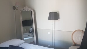Une chambre d’hôtel avec un lit, une table de chevet, un miroir, une lampe et une chaise.