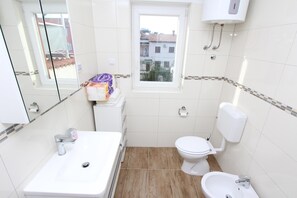A small bathroom with a sink, toilet, bidet, and window. - Apartments Gabriel (Rovinj)