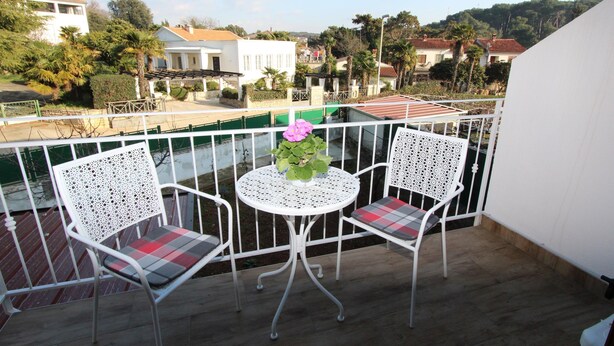 Ein Balkon mit zwei weißen Stühlen und einem Tisch, mit Blick auf eine Wohngegend mit Häusern und Bäumen.
