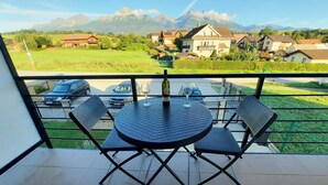 Ein Balkon mit rundem Tisch und vier Stühlen, mit Blick auf eine Wohngegend mit Häusern und Bergen im Hintergrund.