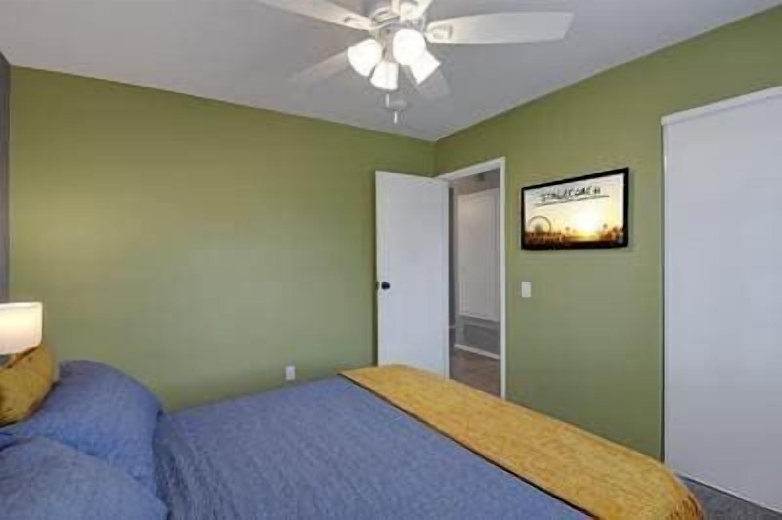 Ein Schlafzimmer mit Bett, Deckenventilator, Tür und einem gerahmten Bild an der Wand.