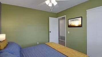 Ein Schlafzimmer mit Bett, Deckenventilator, Tür und einem gerahmten Bild an der Wand.