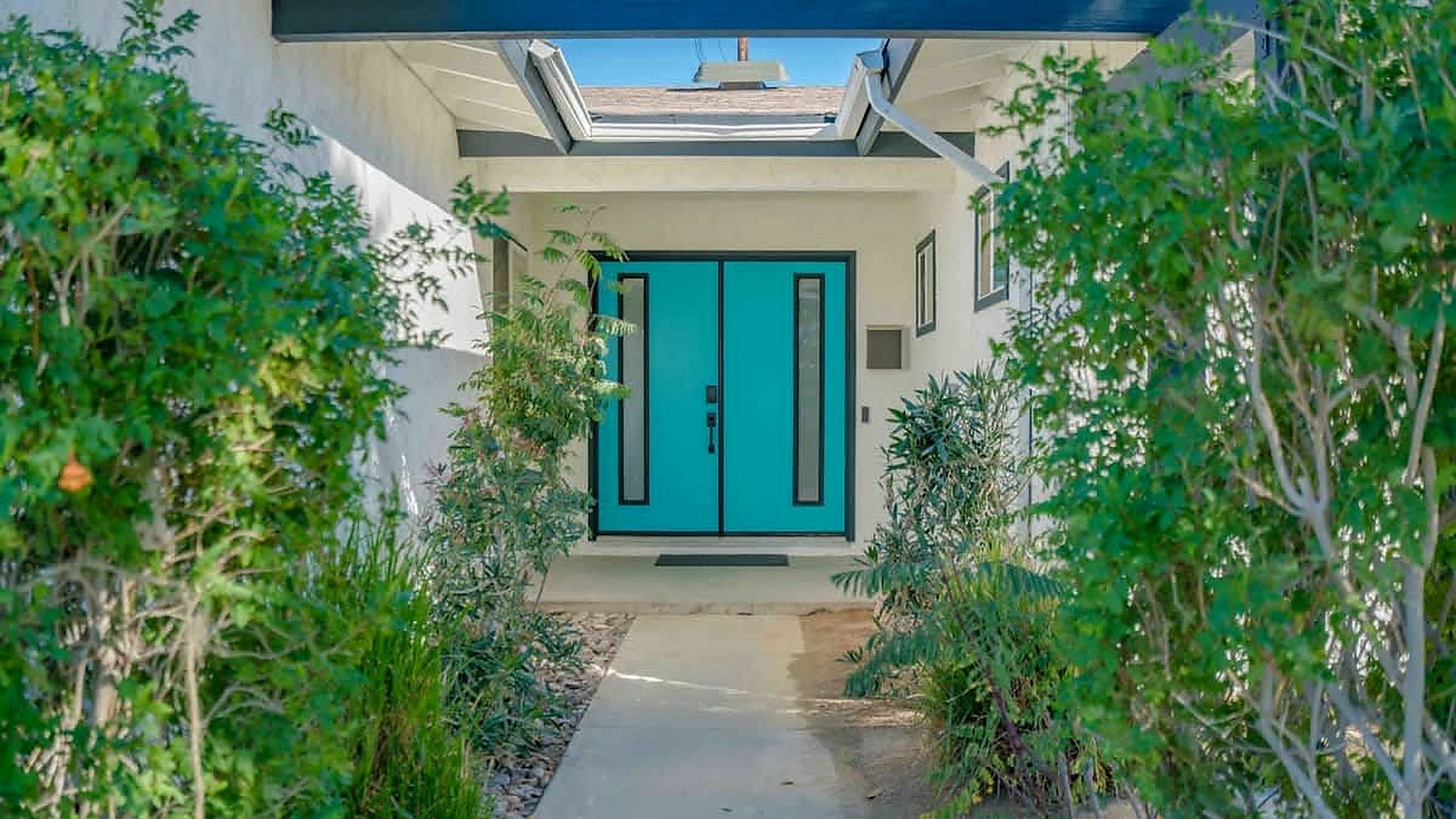Ein modernes Haus mit einer blauen Tür, umgeben von viel Grün.