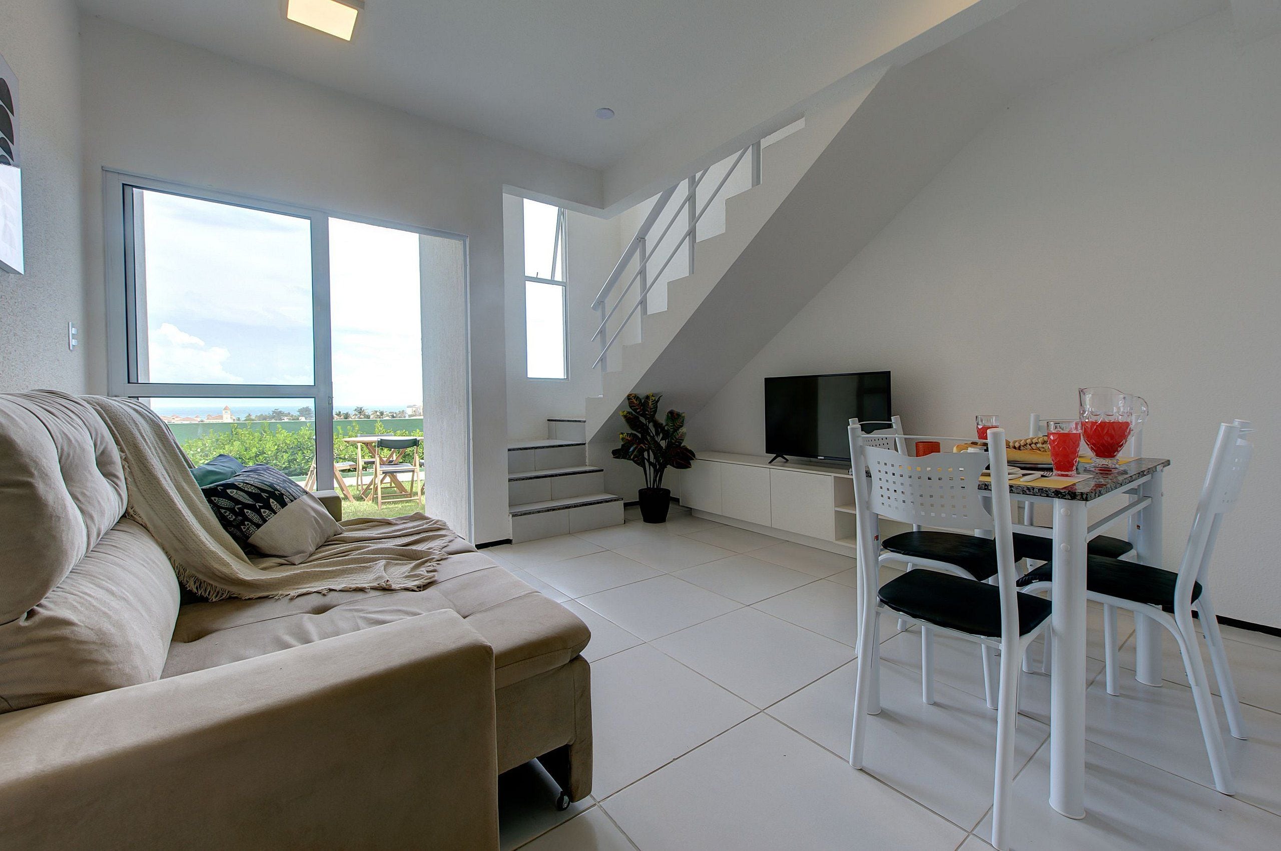 Una sala de estar moderna con sofá, una mesa de comedor con sillas, un televisor y una escalera que sube a un nivel superior.