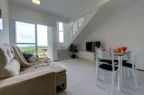 Una sala de estar moderna con sofá, una mesa de comedor con sillas, un televisor y una escalera que sube a un nivel superior.