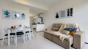 A modern living room with a beige sofa, a dining table with chairs, and artwork on the walls. - Triplex Hidromassagem em Porto das Dunas (Aquiraz)