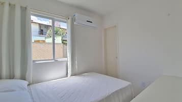 A hotel room with a bed, a window with curtains, an air conditioning unit, and a door.