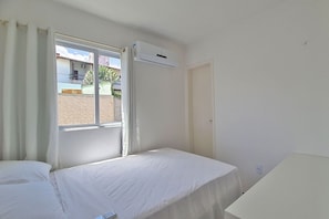 Una habitación de hotel con cama, ventana con cortinas, aire acondicionado y puerta.