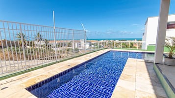 Una piscina con vista al océano, rodeada por una valla y un edificio.