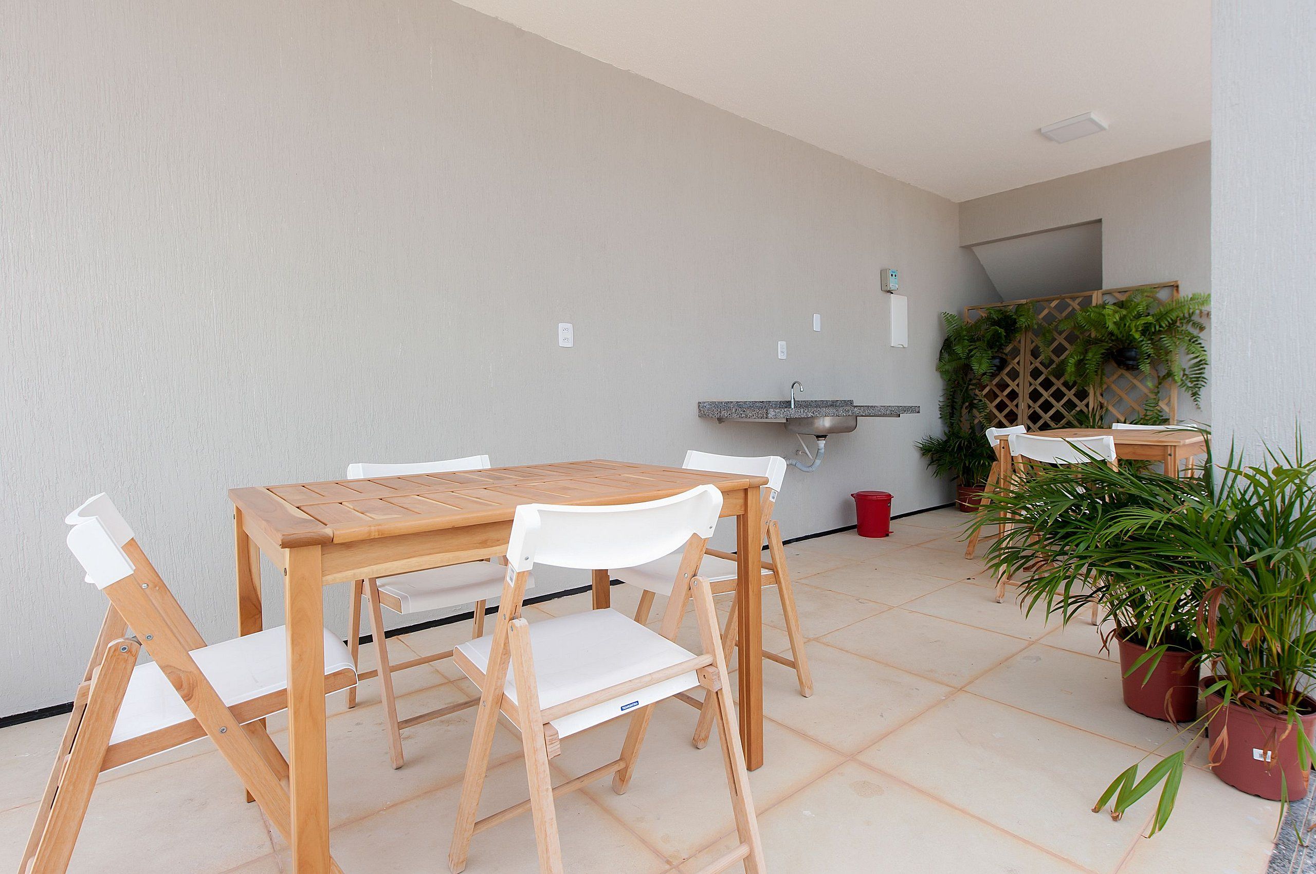 A wooden table and chairs in a room with a tiled floor, a sink, and potted plants.