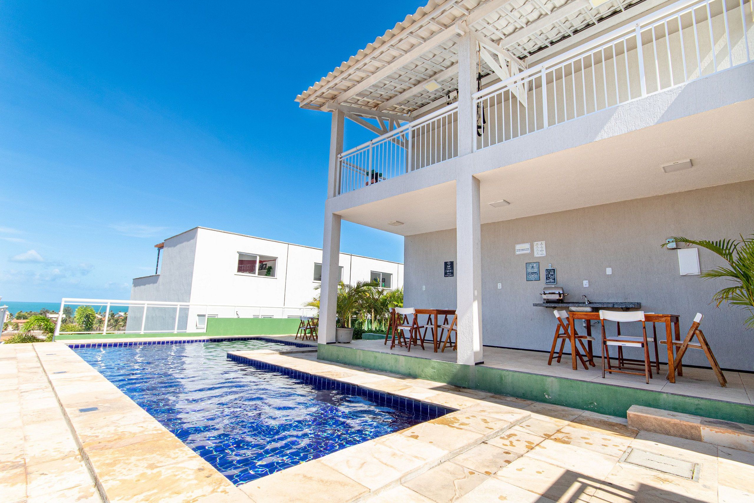 A swimming pool with a patio area, a covered seating area, and a view of the ocean.