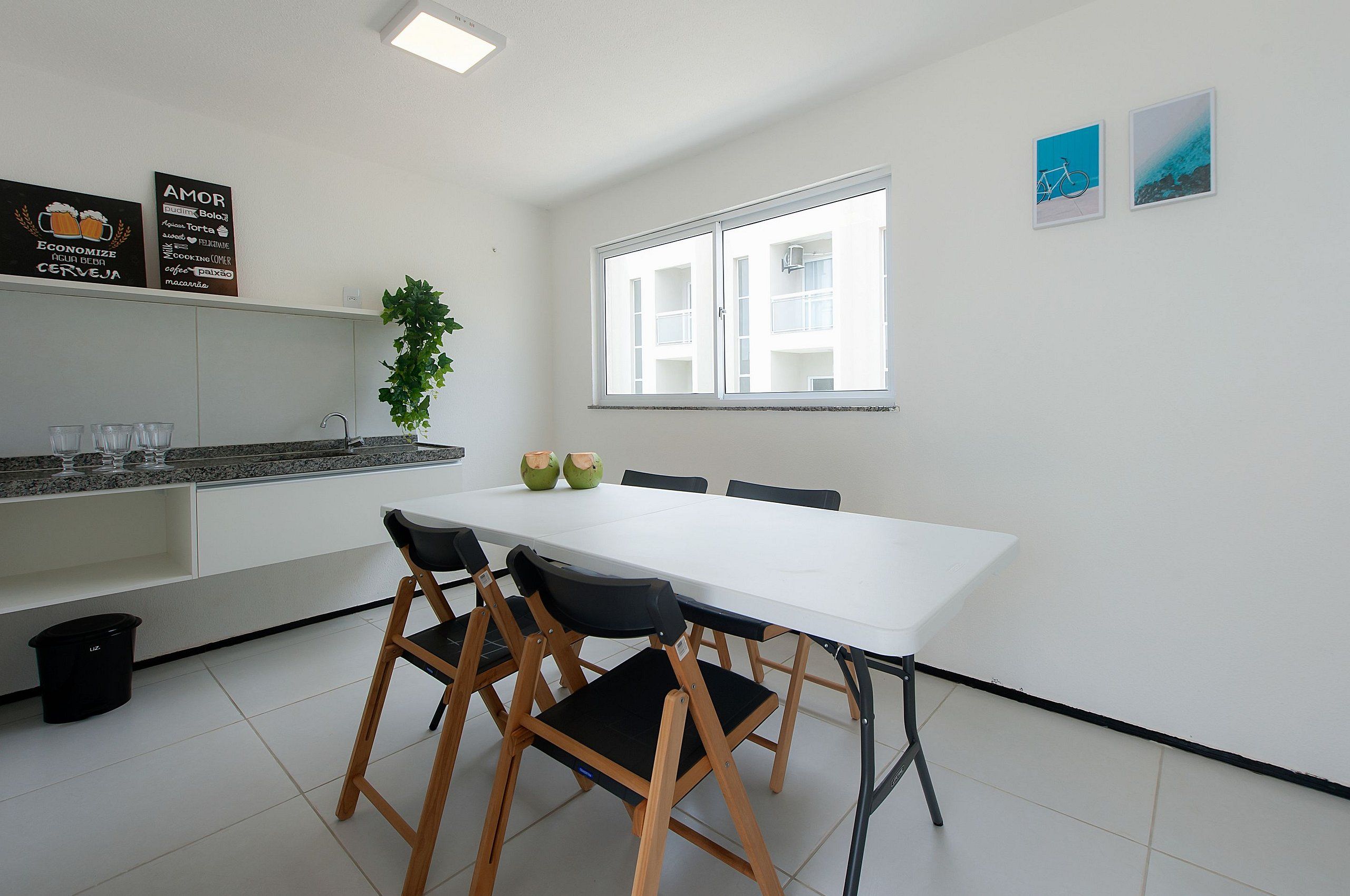 Una cocina moderna con armarios blancos, una mesa de comedor blanca con cuatro sillas y una ventana con vistas a edificios.