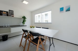 Una cocina moderna con armarios blancos, una mesa de comedor blanca con cuatro sillas y una ventana con vistas a edificios.